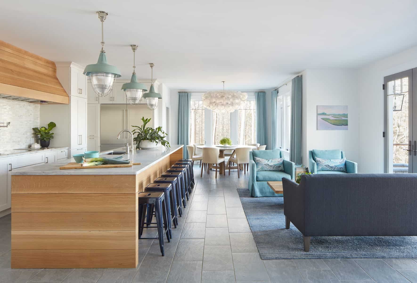Open-concept living room and kitchen with modern decor, light blue and white color scheme, large windows with blue curtains, and various seating areas.