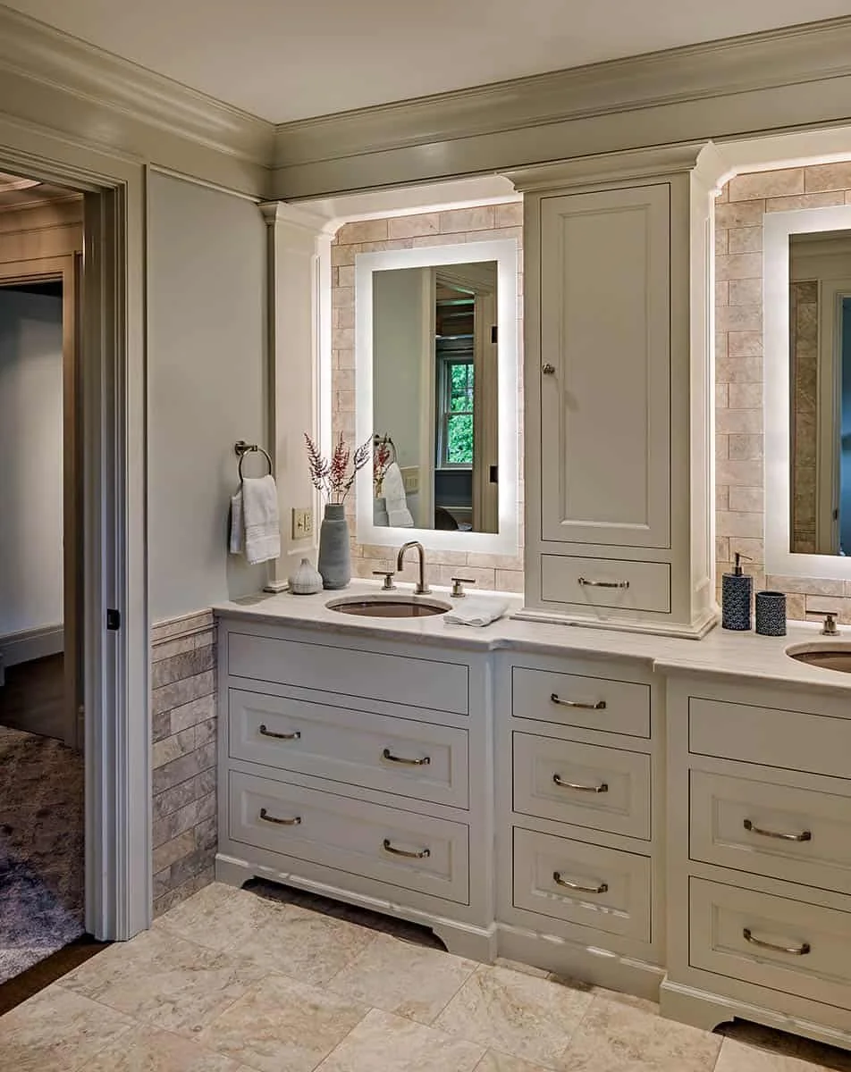 Bathroom vanity with a large mirror, two sinks, and drawers. Decor includes vases with dried flowers and toiletries.