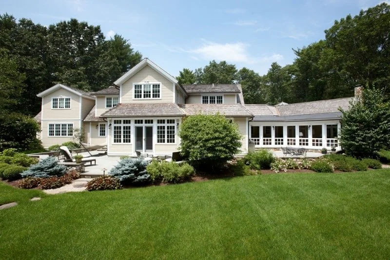 Large two-story house with white exterior, surrounded by a lush green lawn and landscaped garden with shrubs and trees.