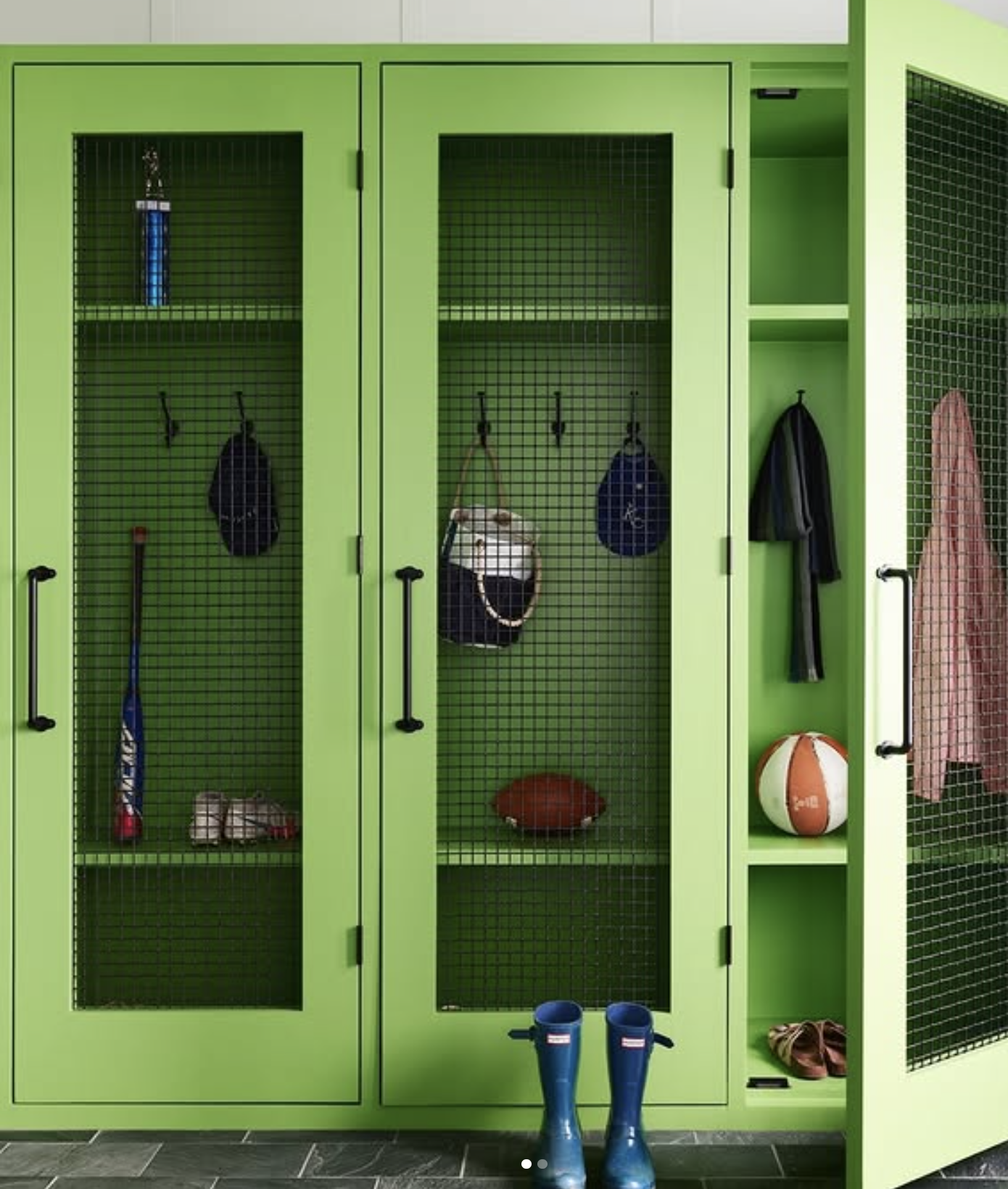 Green organized mudroom locker with mesh doors containing sports equipment, a pair of blue rain boots in front, and shoes on the side shelf.