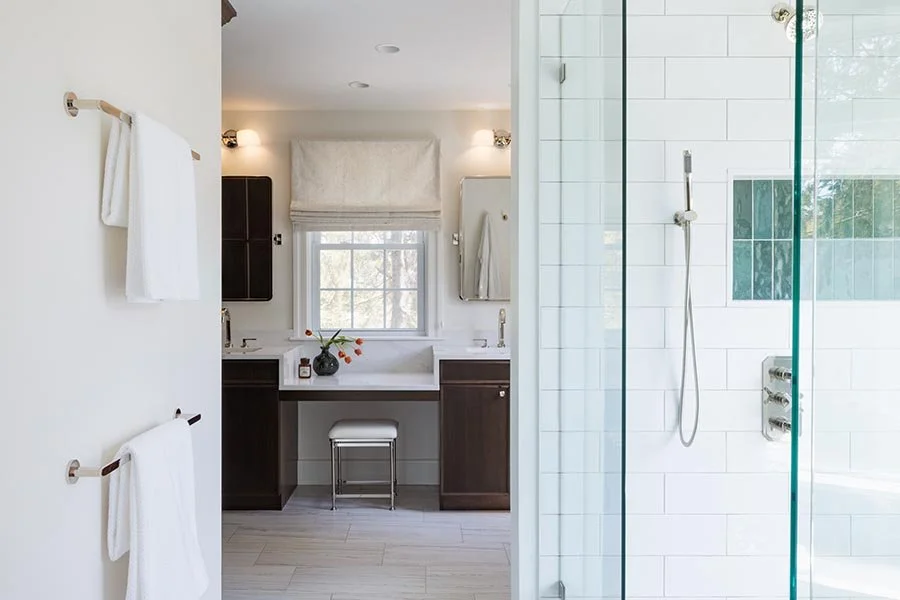 Modern bathroom with a vanity, mirror, window, towels, and a glass-enclosed shower with white tiles.