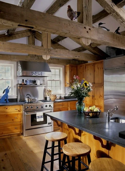 Wooden kitchen with exposed ceiling beams, stainless steel appliances, a bouquet of flowers on the counter, and a bird perched on the ceiling beam.