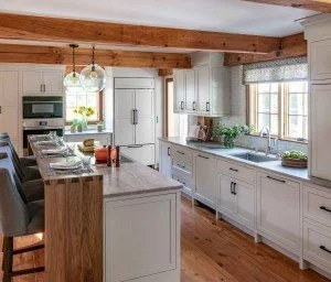 Modern kitchen with white cabinets, marble countertops, wooden beams, and large windows