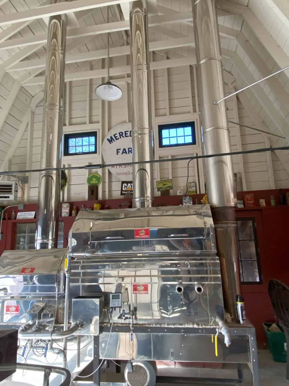 Interior of a barn with large shiny metal equipment, small windows, wood paneling, and signs indicating Meredeth Farms.
