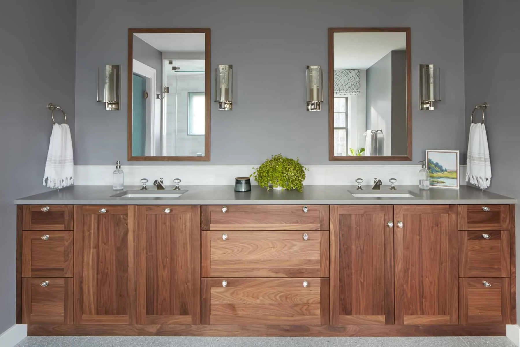 Double bathroom vanity with wooden cabinets, two mirrors, two sinks, and wall-mounted light fixtures, with towels and decorative items.