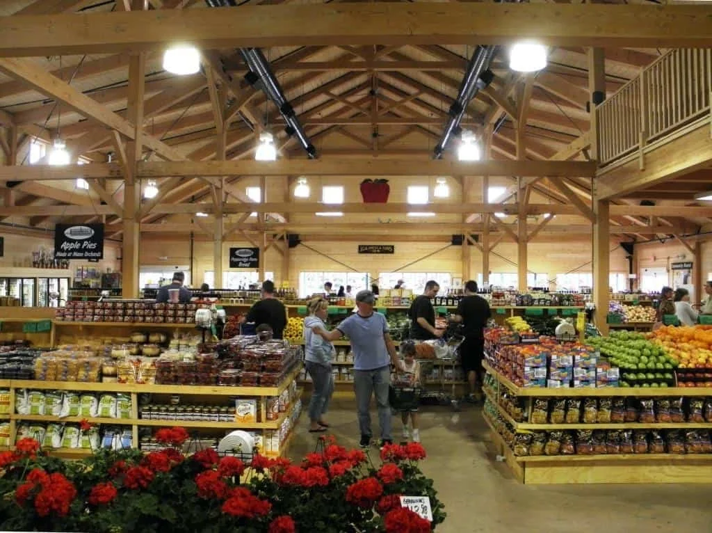 Inside a grocery store with wooden beams, several customers shopping for fruits and vegetables.