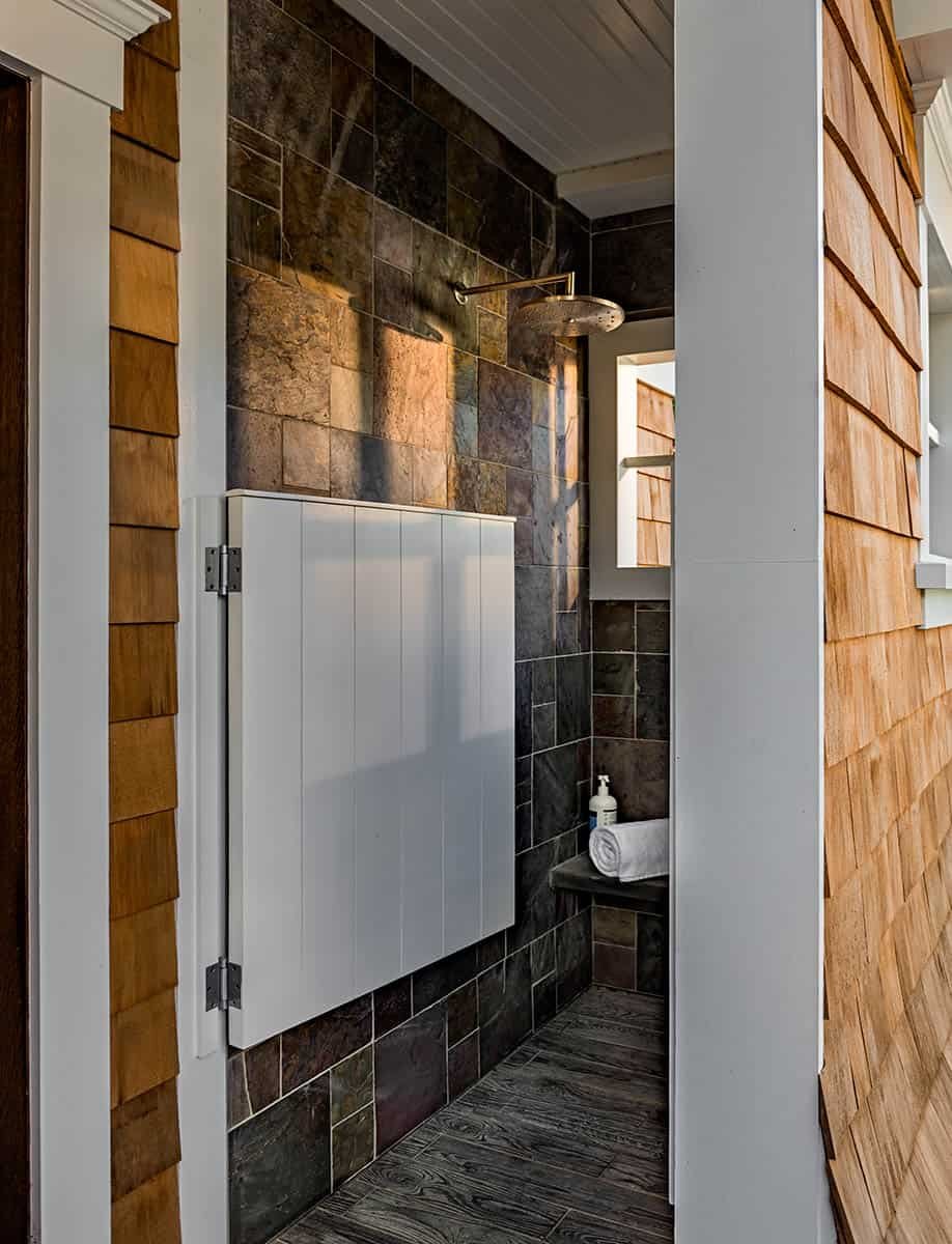 A small outdoor shower area with slate tile walls and a rain showerhead, partially enclosed by wooden siding and a white wall.