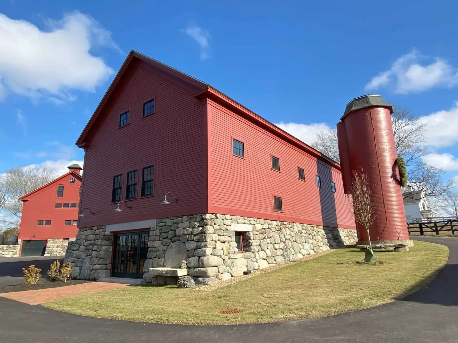 Red barn with a stone foundation and a red silo against a blue sky with some clouds.
