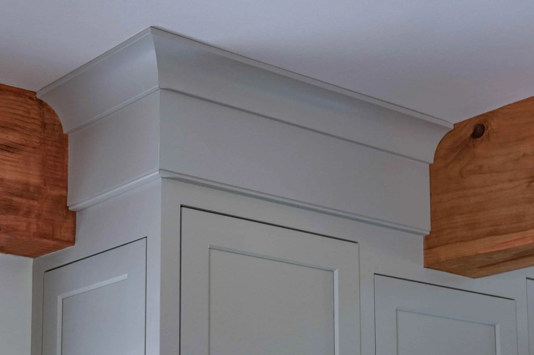 Interior wall corner with white crown molding and two wooden beams on the ceiling, one on each side.