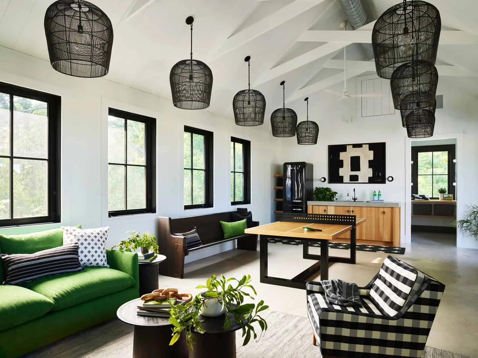 Living room with green sofa, black and white striped armchair, black pendant lights, modern art on the wall, and several windows letting in natural light.