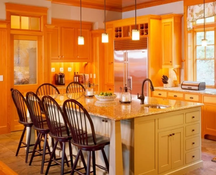 Bright kitchen with yellow wooden cabinets, granite countertop island, black bar stools, stainless steel refrigerator, large window, and pendant lighting.
