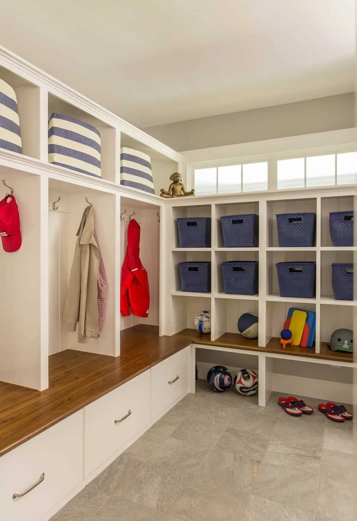 A mudroom with hooks for hanging coats and hats, blue storage bins in cubbies, and sports equipment including soccer balls, sneakers, and sandals.