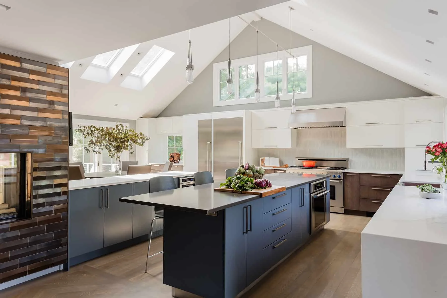 Modern kitchen with white and dark wood cabinetry, a blue island, stainless steel appliances, and natural light from skylights and windows.