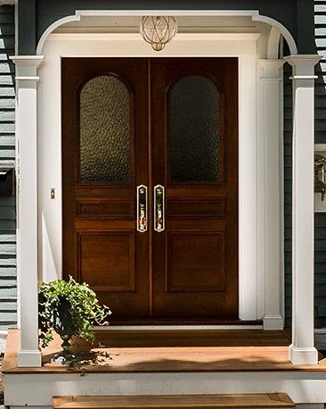 Front double wooden door with glass panels, framed by white porch columns and arch, with a hanging light fixture above.