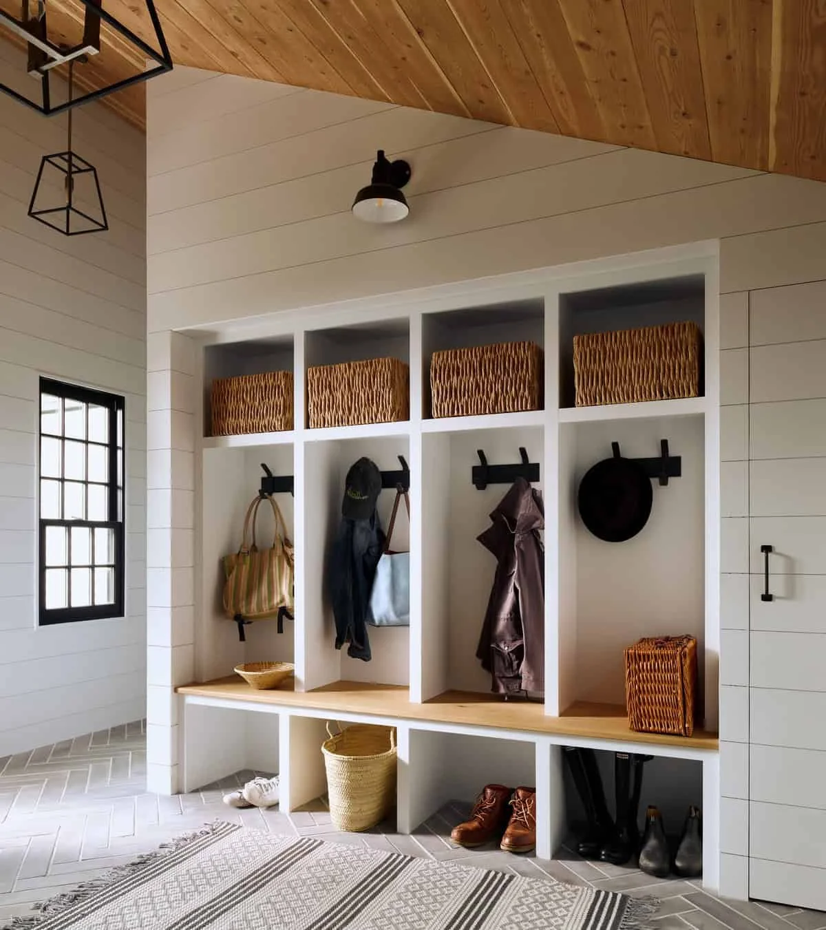 Mudroom with white built-in cubbies and hooks, decorated with baskets, hats, jackets, bags, and shoes.
