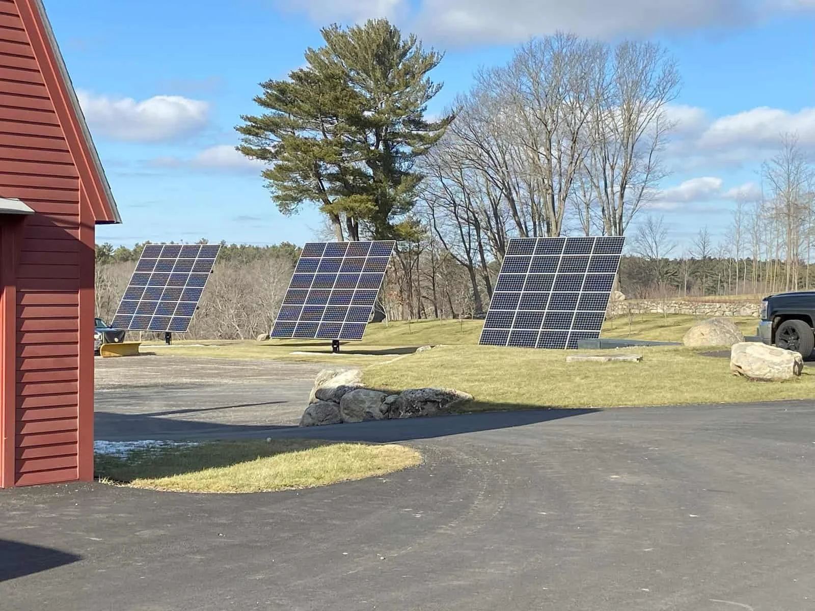 Three solar panel arrays outdoors on a grassy area near trees with a partly cloudy sky.