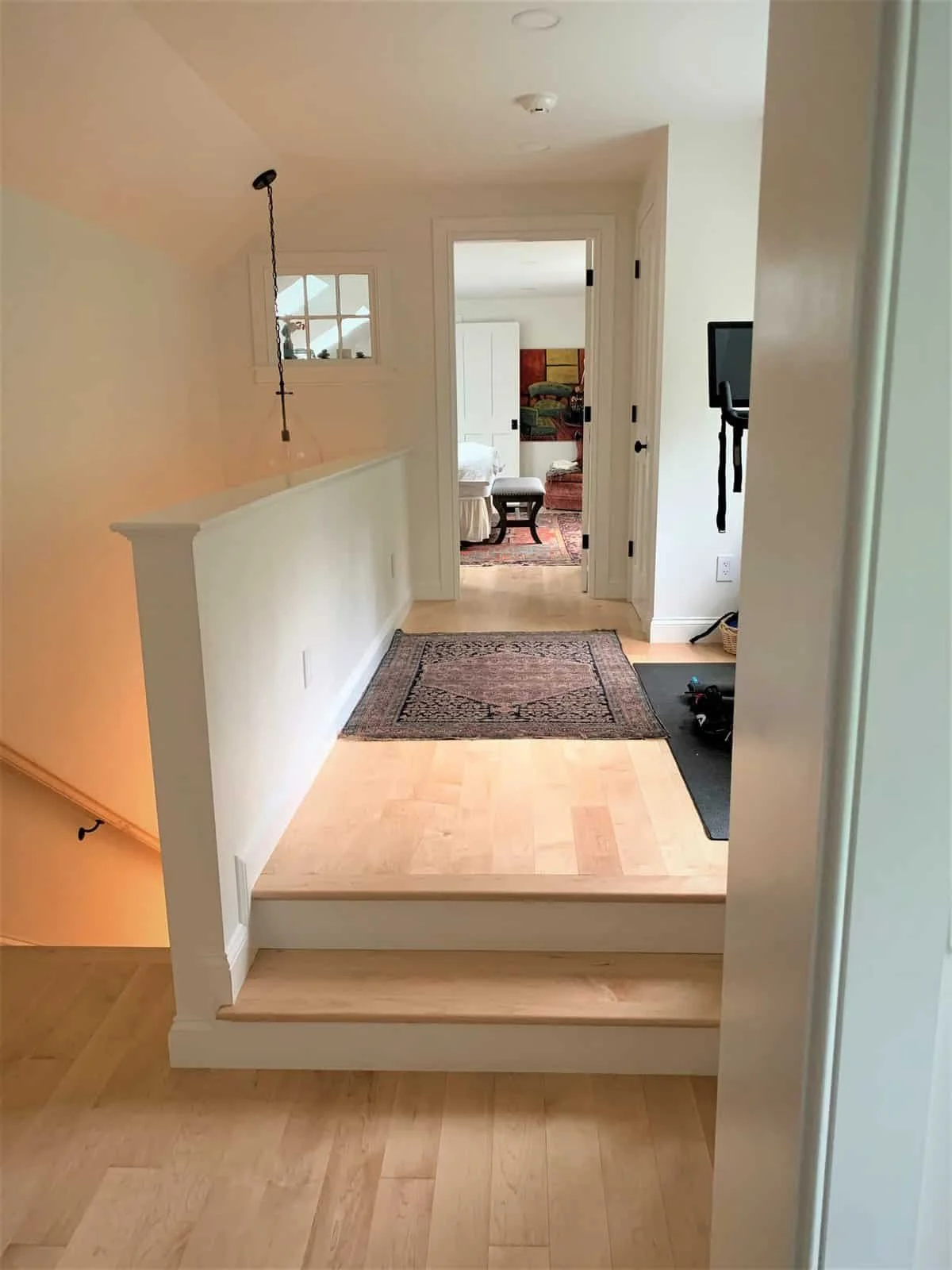 View of a hallway with a small step up from the lower level, leading to a landing with a rug, and a doorway opening into a room with furniture and a colorful painting on the wall.