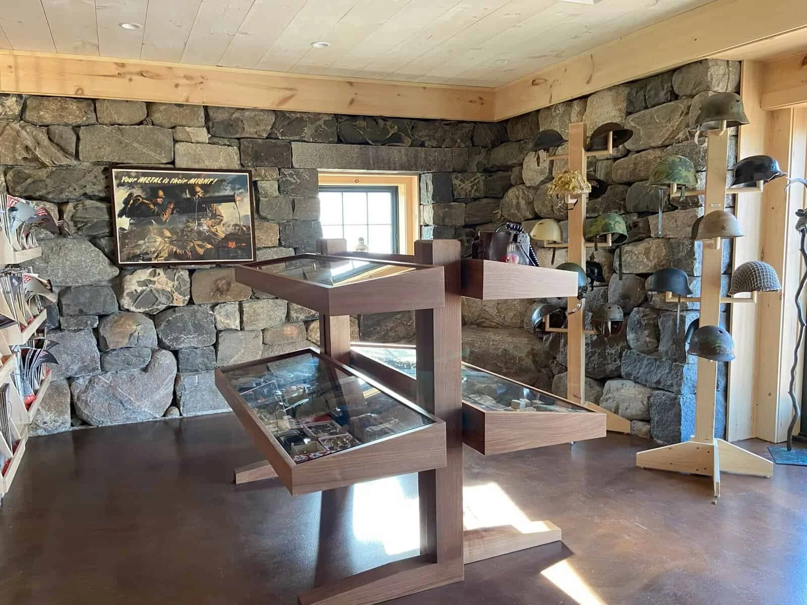 A room with a stone wall, display cases, and a helmet stand with military helmets.