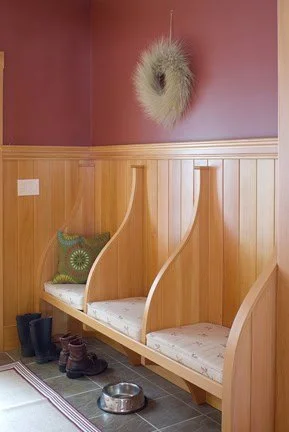Coat hooks with a cushion and boots underneath, with a wooden wall and a decorative wreath on a painted wall.