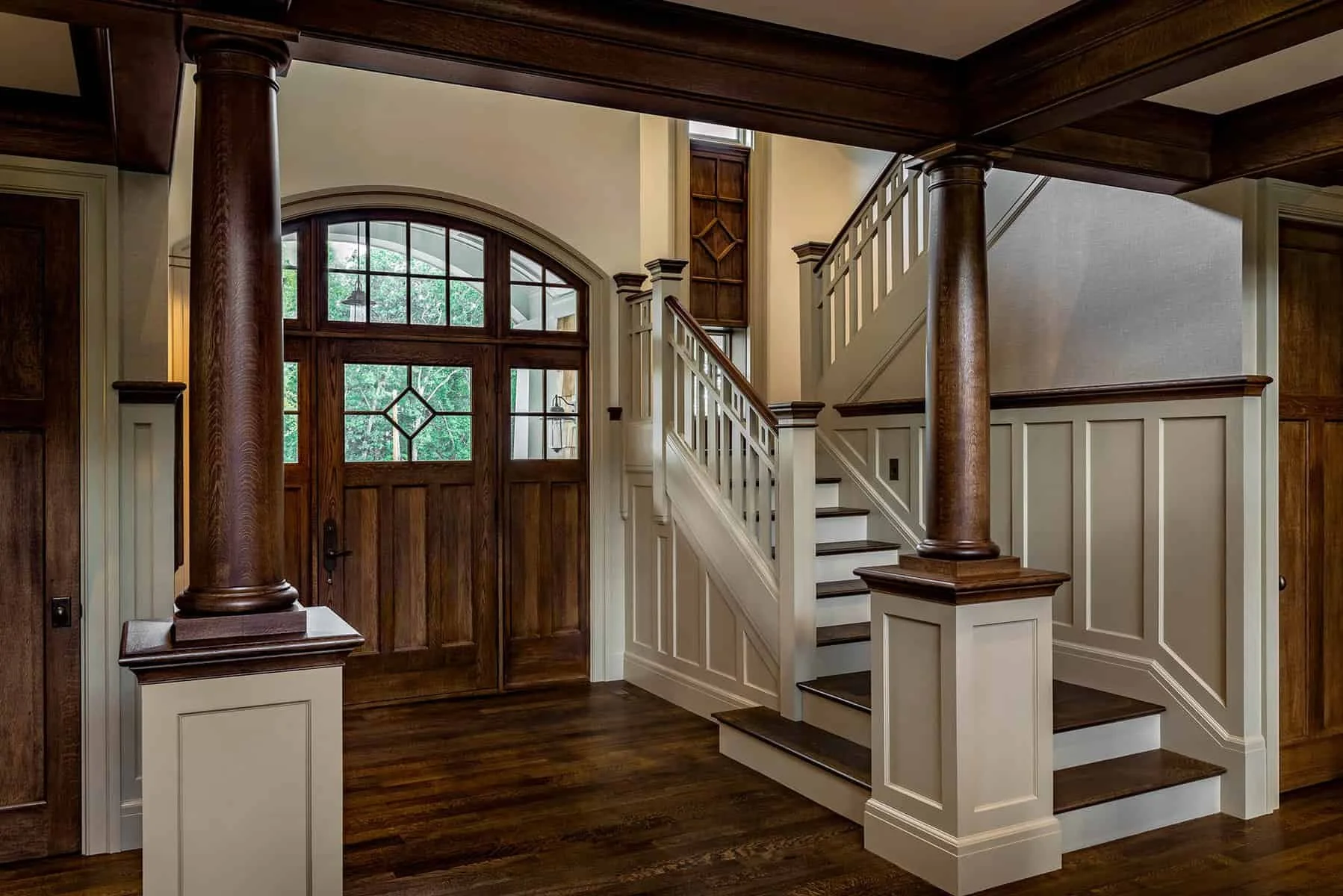 Front entryway with wooden door and staircase, featuring large wooden columns and white paneled walls.