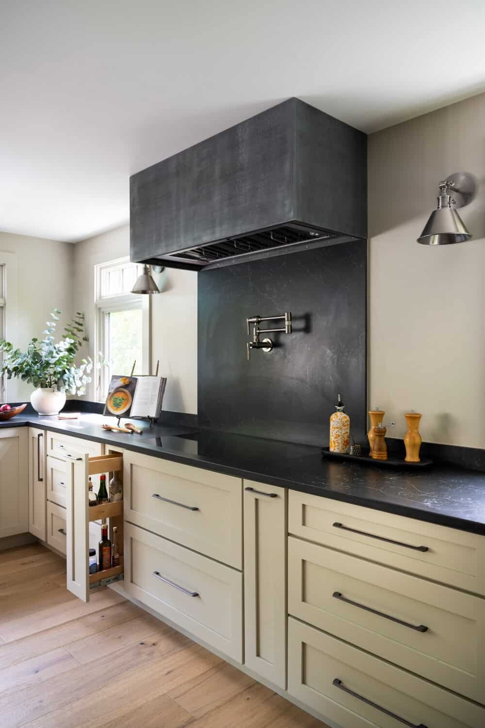 Modern kitchen with black countertop, white cabinets, wall-mounted faucet, and a dark gray range hood