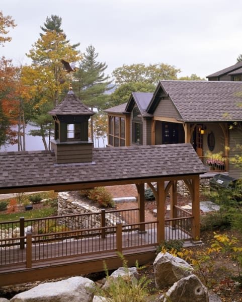 A backyard with a wooden deck and gazebo, overlooking a lake with trees displaying autumn colors.