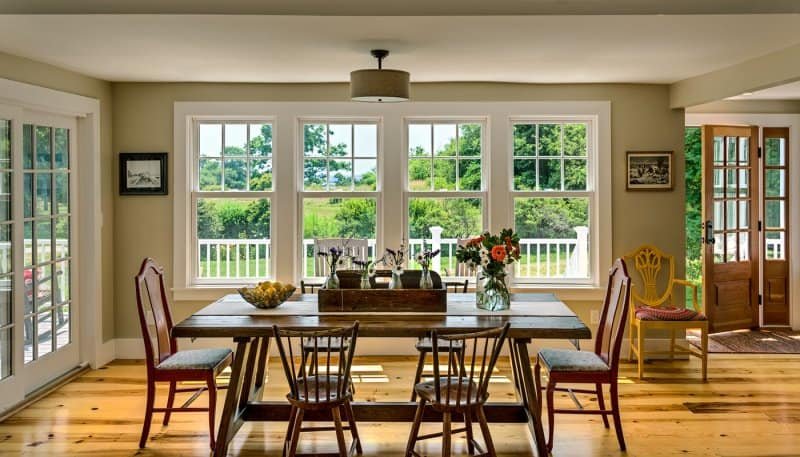Bright dining room with large window overlooking a lush, green outdoor landscape, wooden dining table, and chairs, with a door leading outside.