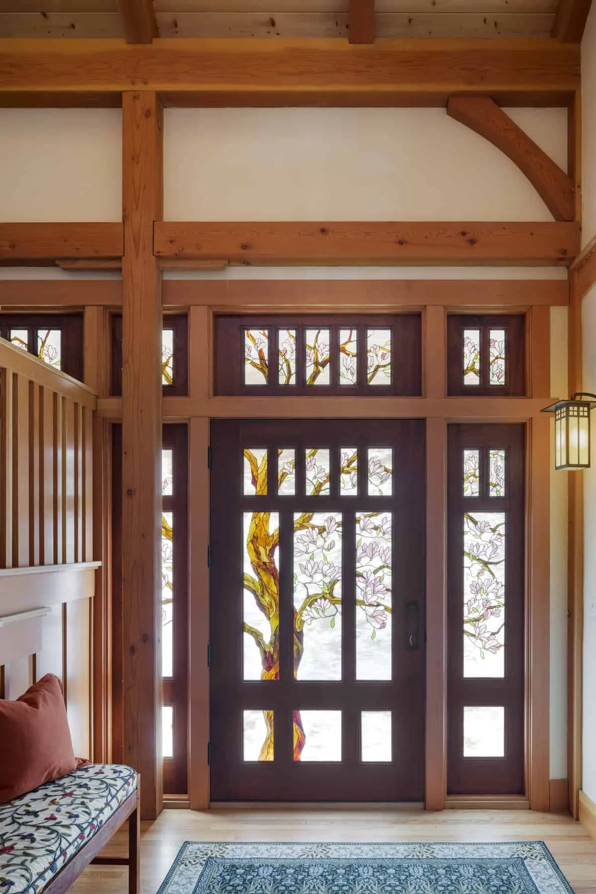 Wooden interior entryway with stained glass door featuring a tree and floral design, wooden beams, and a patterned rug.