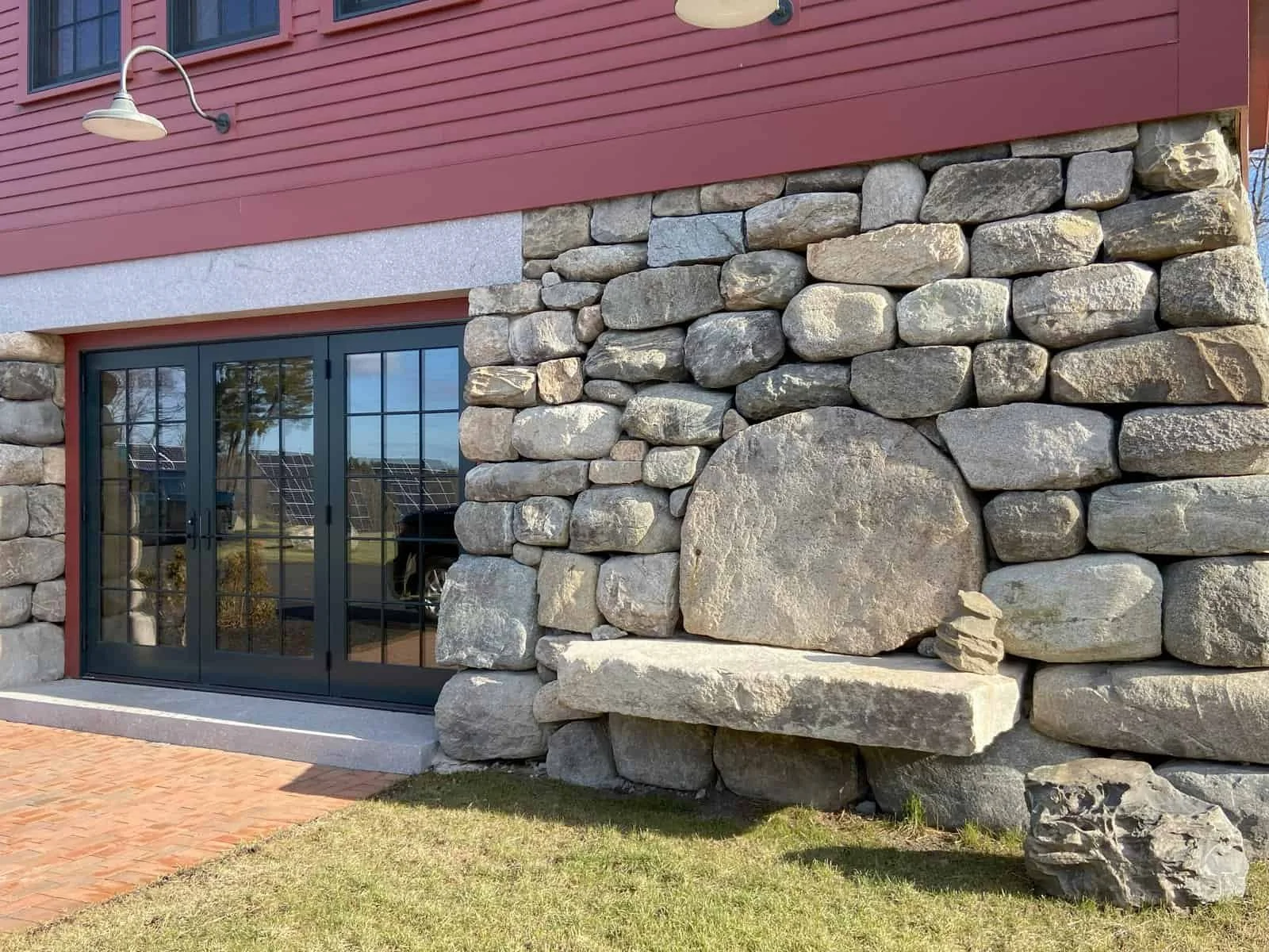 Exterior of a building with a stone wall, large stone feature, glass sliding door, red siding, and a porch light.