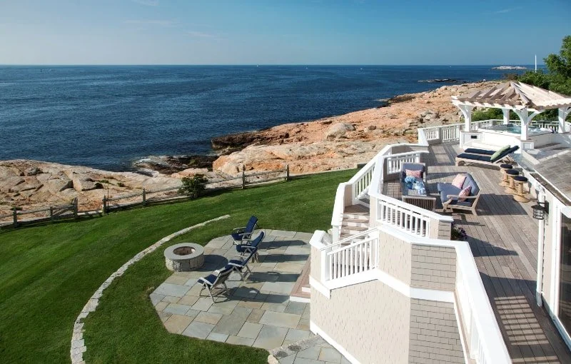 Coastal outdoor patio with seating area, fire pit, and ocean view with cliffs and blue sky in the background.