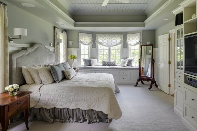 Bright bedroom with a large bed, window seat with pillows, and a standing mirror.