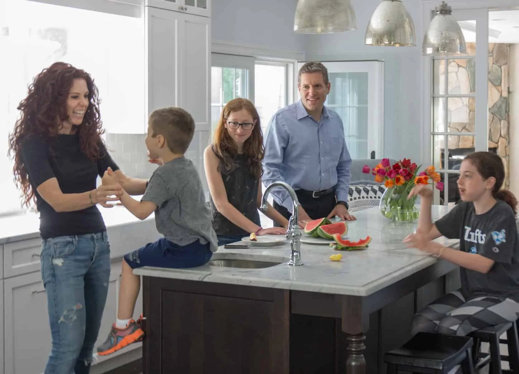 A family scene in a modern kitchen with a large fabulous functional island with beautiful lights above it. 