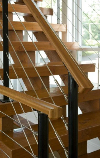Wooden staircase with metal railings near a large window with a view of greenery outside.