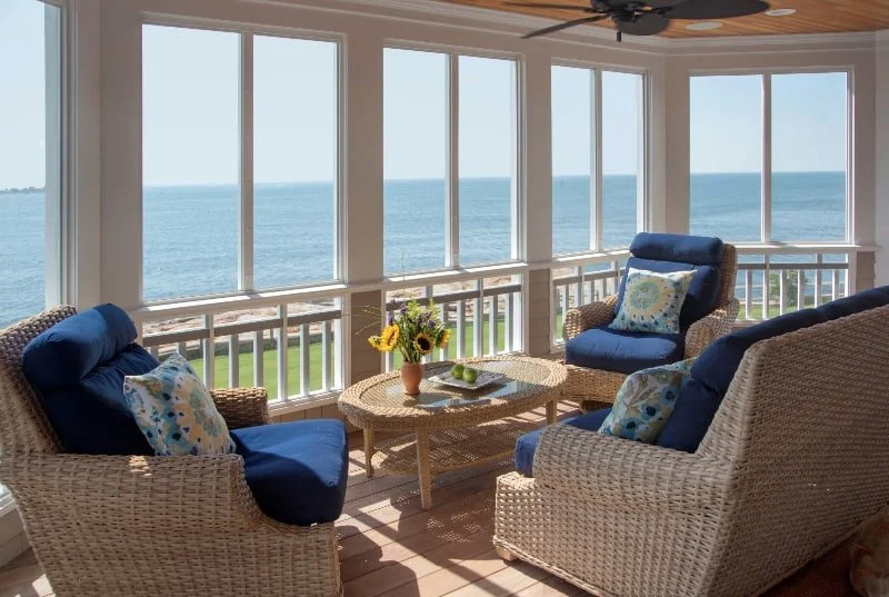 Sunroom with wicker furniture and blue cushions overlooking the ocean.