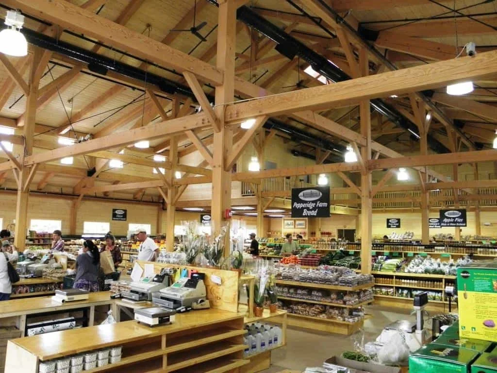 Interior view of a grocery store with wooden beams on the ceiling, shelves stocked with various produce and packaged goods, and customers shopping.