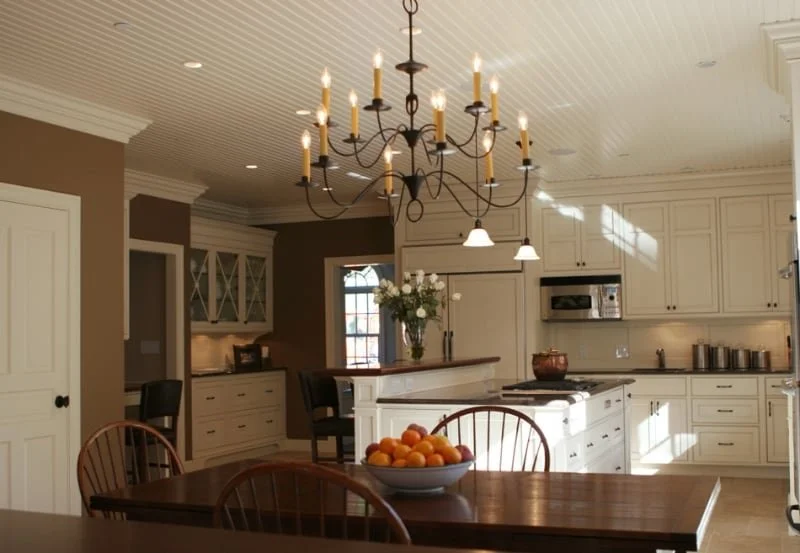 Bright kitchen with white cabinets, a refrigerator, microwave, and a chandelier hanging above a dining table with a bowl of oranges.