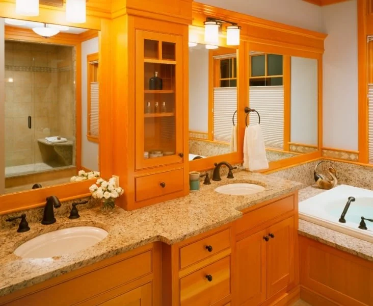 Bathroom with dual sinks, granite countertops, large mirror, and a bathtub. Wooden cabinetry and a glass-enclosed shower are also visible.