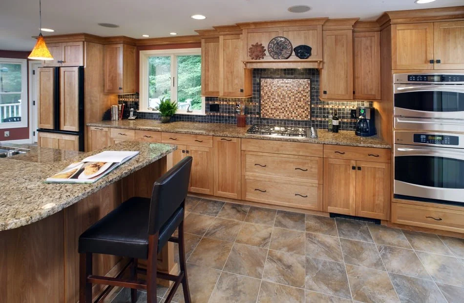Kitchen with wooden cabinets, granite countertops, a double oven, black appliances, a window overlooking greenery, and tiled flooring.
