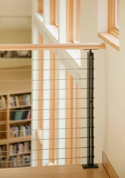 Interior view of a stairway with a wooden handrail and a black metal spindled balustrade, next to windows with natural light.