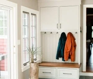 Entryway with white cabinets, hooks with coats, a small table, and windows letting in natural light.