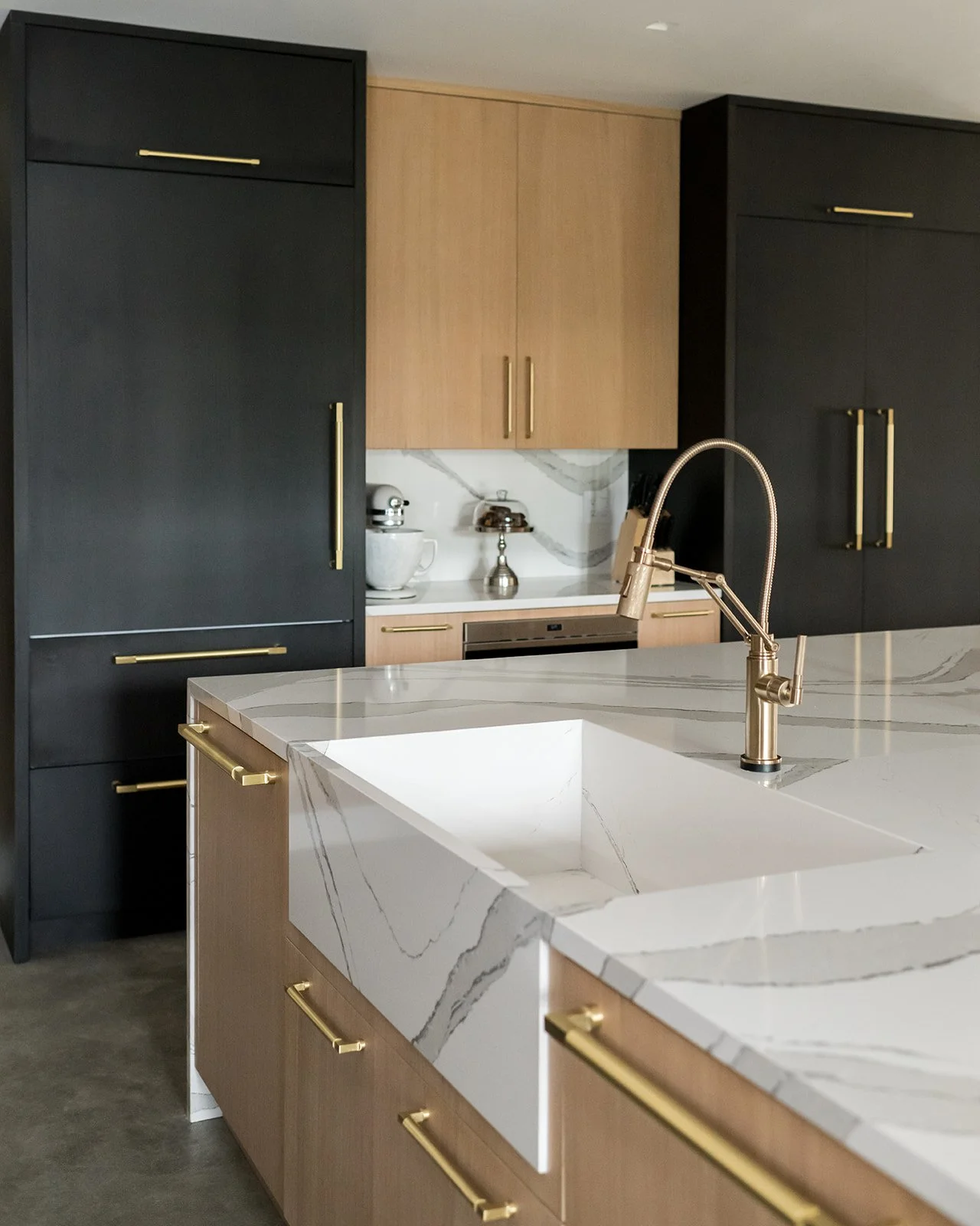 Contemporary kitchen with white marble island, gold handles, black and wooden cabinets, and a modern kitchen faucet.