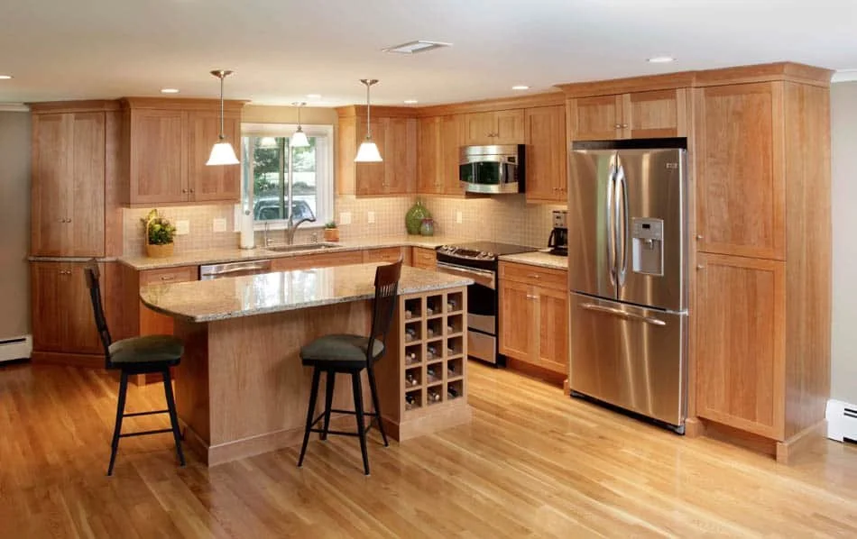 Modern kitchen with wooden cabinets, stainless steel refrigerator, oven, microwave, and a kitchen island with two bar stools.