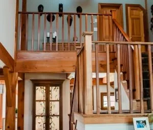 Interior view of a wooden staircase with railing, leading to an upper floor in a house. The staircase features decorative elements and a door at the bottom.