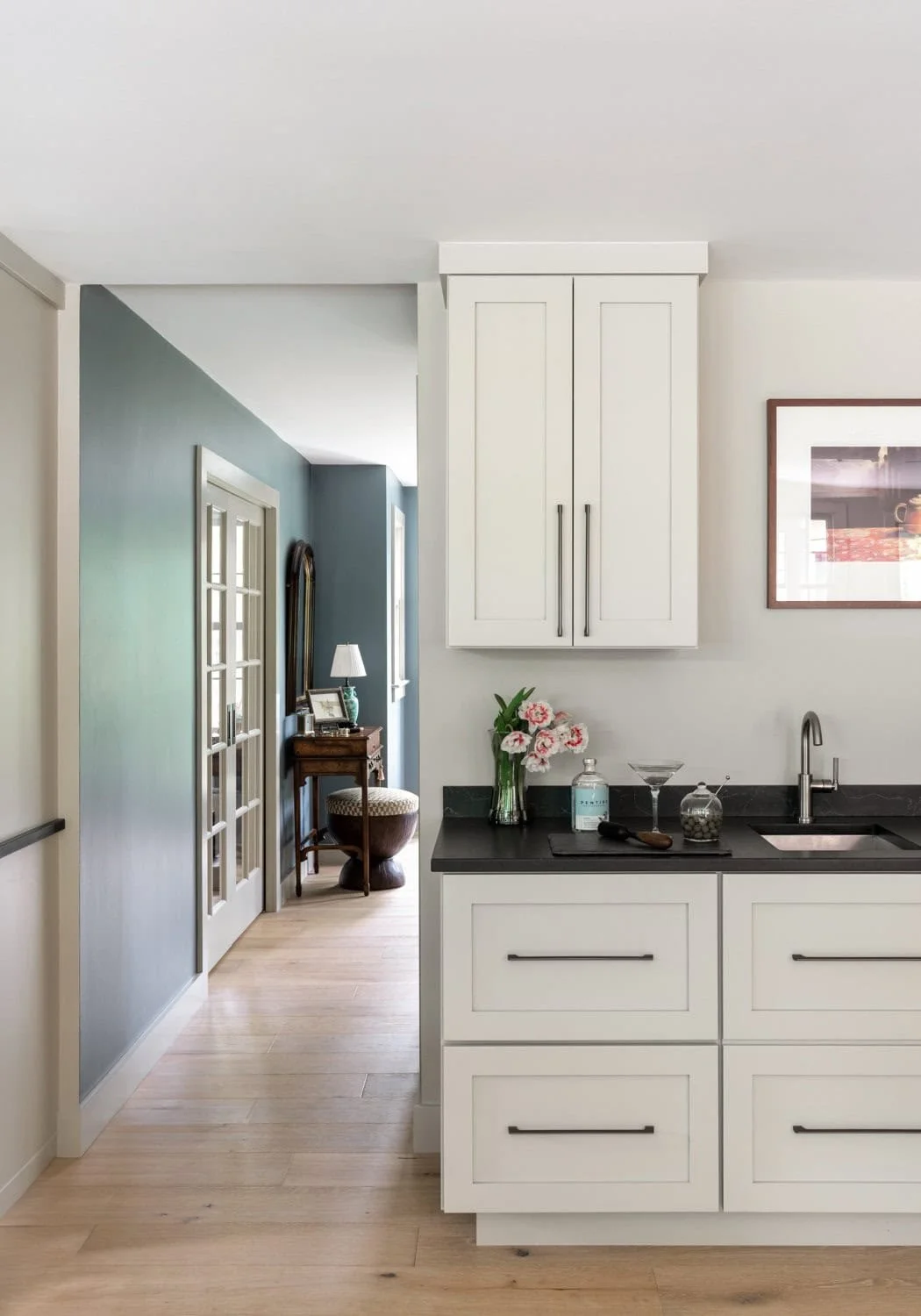 Interior view of a modern kitchen with white cabinets, black countertops, a vase of pink and white flowers, a martini glass, and a small jar.