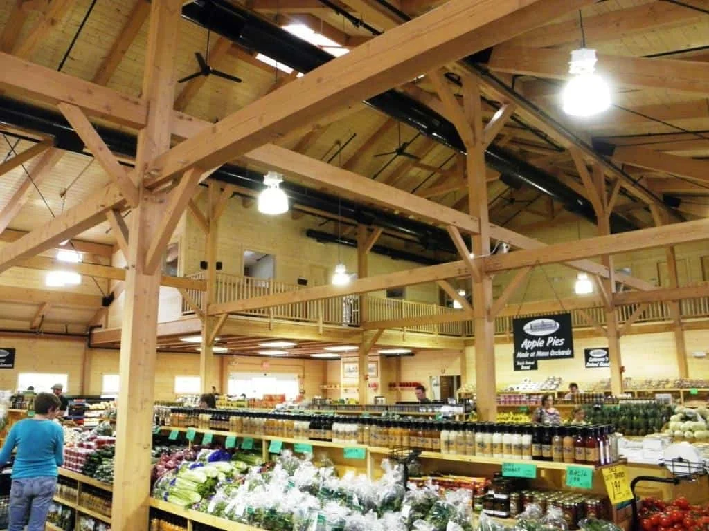 Inside a grocery store with wooden beams and shelves full of produce and jars, shoppers browsing.