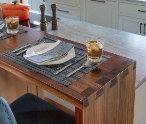A wooden kitchen table with a blue and white striped placemat, a napkin, and two glasses of iced tea with lemon slices.
