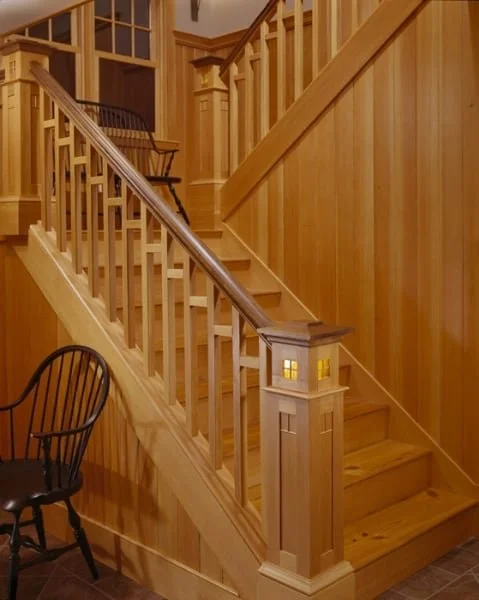 Wooden staircase with a handrail, newel post, and spindles in a well-lit interior space.