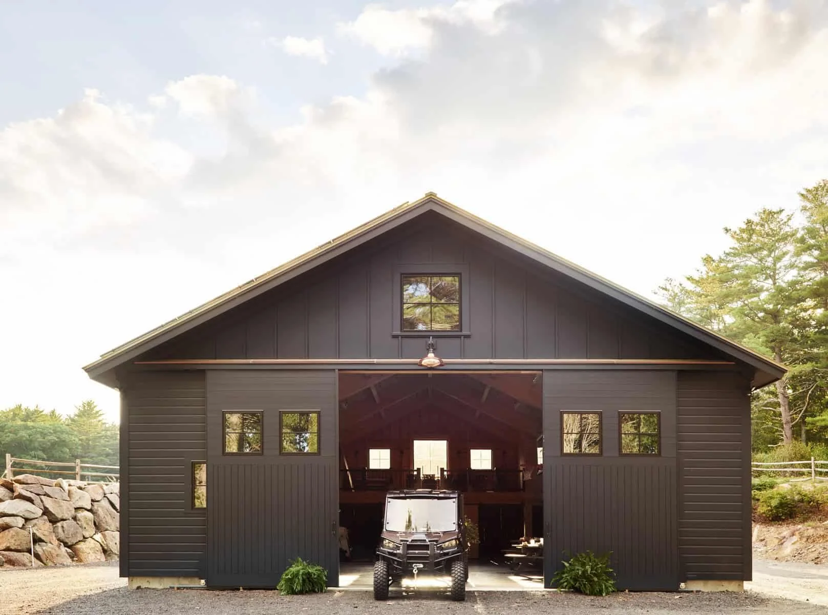 Black barn with open garage door, a black ATV inside, and trees in the background.