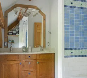 Bathroom with a large mirror above the sink, wooden cabinets, and a tiled shower area with blue and white tiles.