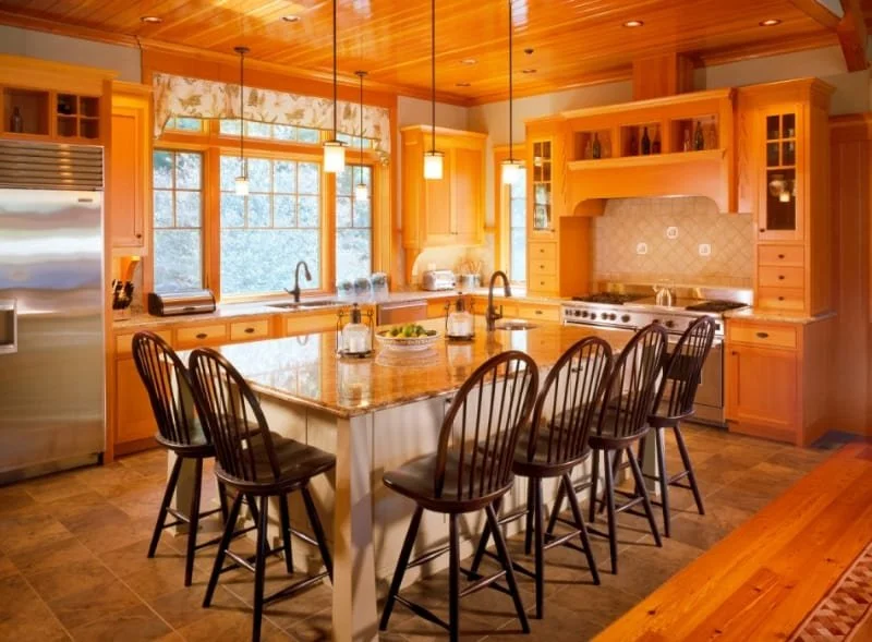 Bright kitchen with wooden cabinets, a large island with bar stools, stainless steel appliances, and a window overlooking nature.